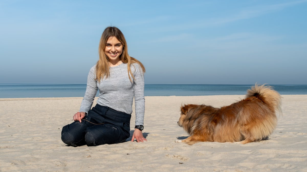 A woman playing with her dog on the sandy beach of Kołobrzeg on a sunny day.